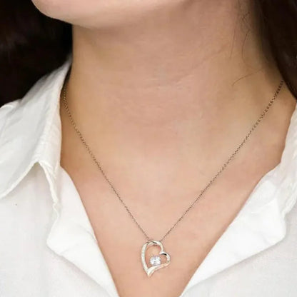 Silver heart-shaped necklace with a central gemstone worn by a person against a white shirt.